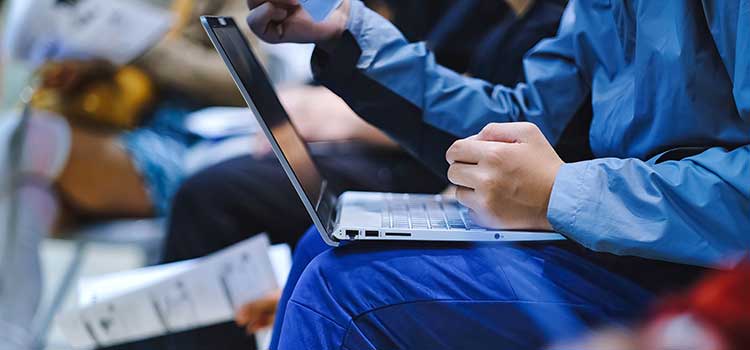 college student with laptop on knees in crowded computer bootcamp